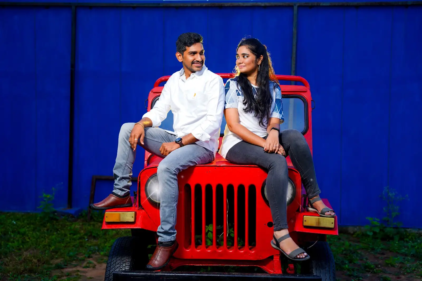 Couple seated on vintage red jeep at pre wedding shoot studio in Hyderabad