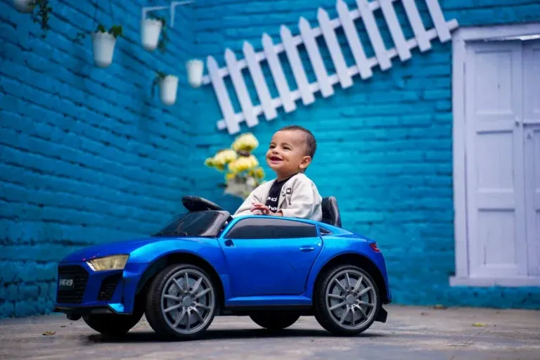 Baby in blue toy car against blue brick wall – baby photoshoot in Hyderabad